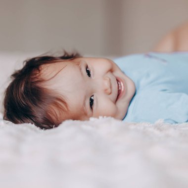 sevimli gülen bir yaşındaki kız yatakta yatan ve kamera bakarak ayaklarına dokunmak