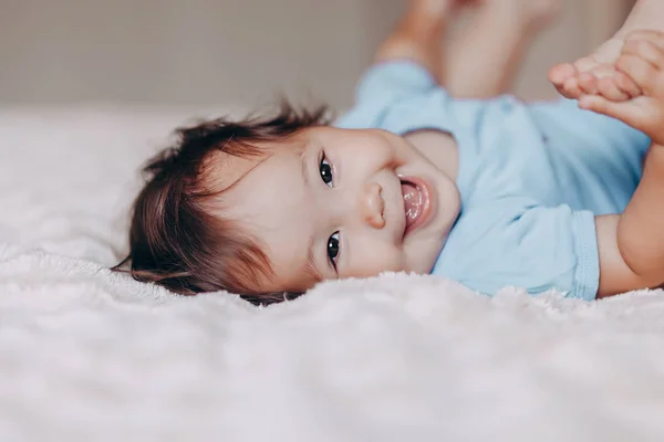 Sevimli gülen bir yaşındaki kız yatakta yatan ve kamera bakarak ayaklarına dokunmak — Stok fotoğraf