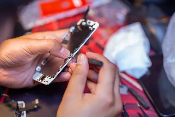 A man is repairing a mobile phone. In the frame, his hands and details of the device. repair shop for gadgets