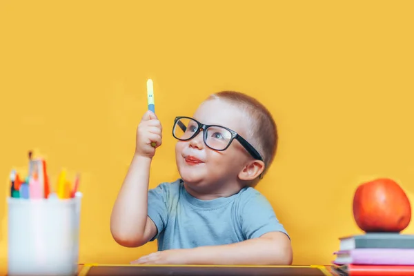 小さな男の子が絵を描き、彼の机の上で宿題をして、アイデア、インスピレーションの概念を持っています。黄色の背景で学校に戻る — ストック写真