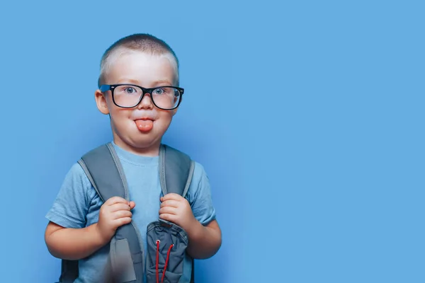 Back to school blonde boy show tongue with school bag on shoulders in glasses show tongue — Stock Photo, Image