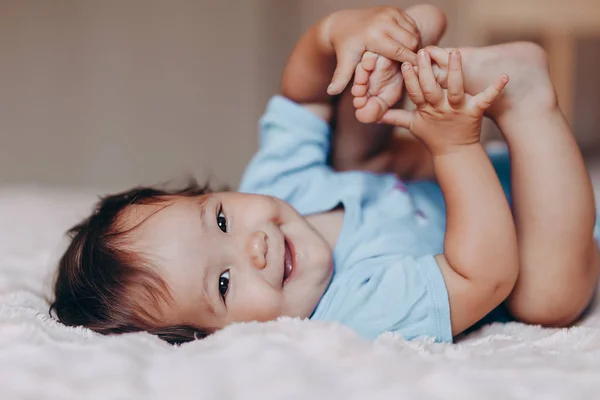 Schattig lachen een jaar oud meisje liggend op bed en kijken naar camera aanraking haar voeten — Stockfoto