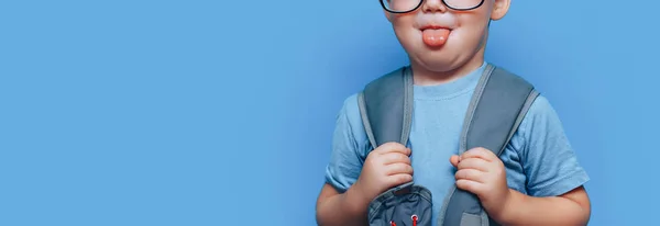 Back to school blonde boy show tongue with school bag on shoulders in glasses show tongue — Stock Photo, Image