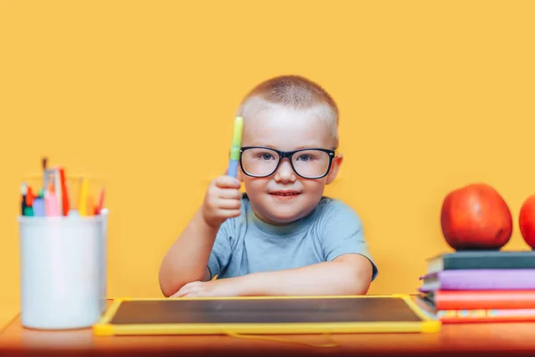 Маленький хлопчик малює і робить домашнє завдання на своєму столі, маючи ідею, концепцію натхнення. назад до школи на жовтому фоні — стокове фото