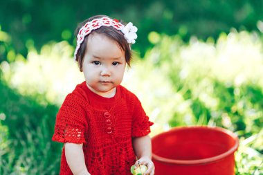 Güzel bir çiçeklenme meyve bahçesinde piknik zevk kırmızı bir elbise giyen örgü çiçek taç ile sevimli mutlu yürümeye başlayan kız