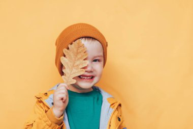 Sonbahar. Mutlu çocuk sonbahar yaprağı ile gözleri kapalı. Sonbahar zamanı. Elinde sarı yapraklar olan gülümseyen bebek. Mevsimlik moda. Sonbahar kıyafetleri. çocuk modası. Yaprak düşmesi. altın klother çocuk, turuncu şapka