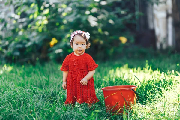 Очаровательная счастливая девочка с вязаной цветочной короной в красном платье, наслаждающаяся пикником в красивом цветущем фруктовом саду — стоковое фото