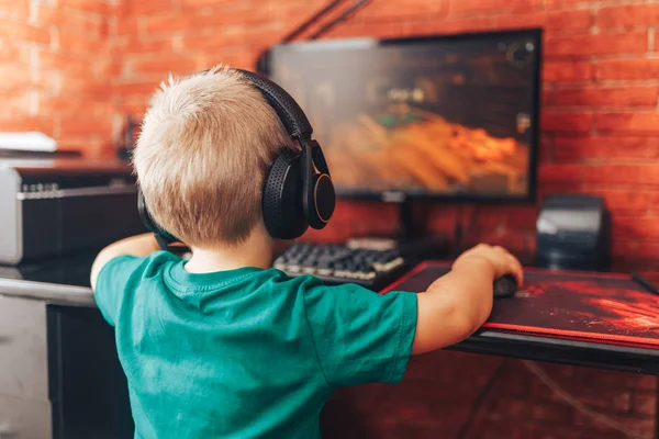 Niño jugando juegos en el ordenador en auriculares con micrófono, juego de ordenador — Foto de Stock