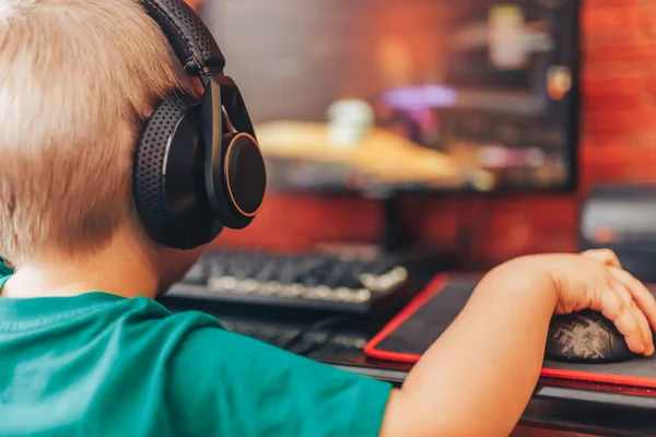 Niño jugando juegos en el ordenador en auriculares con micrófono, juego de ordenador — Foto de Stock