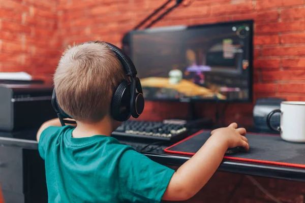 Niño jugando juegos en el ordenador en auriculares con micrófono, juego de ordenador —  Fotos de Stock