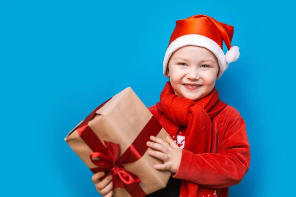 Retrato de un niño feliz sosteniendo un nuevo regalo de Navidad con cinta roja en ropa roja. feliz año nuevo, feliz Navidad —  Fotos de Stock