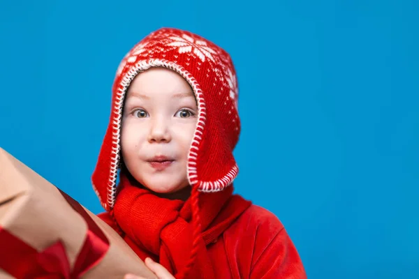 En Navidad. niño con Santa Claus Sombrero celebración de regalo de Navidad con cinta roja y wery cara sorprendida con la boca abierta —  Fotos de Stock