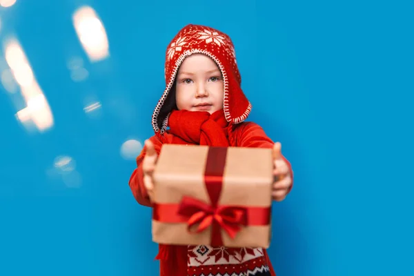 Niño pequeño llevar traje de santa sonrisa y mostrar caja de regalo con lazo rojo sobre fondo azul. enfoque seleccionado. tiempo de Navidad —  Fotos de Stock