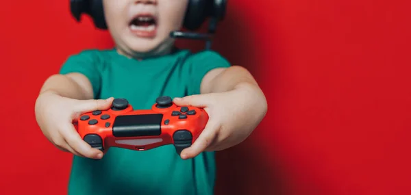 Menino pequeno em fones de ouvido e joystick no fundo vermelho — Fotografia de Stock