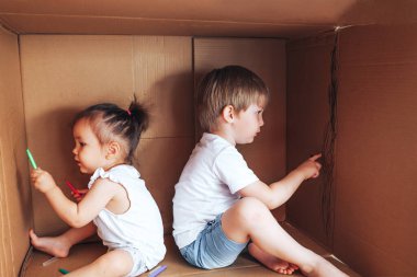 Keçeli kalemle resim çizen ve kutuda oynayan güzel çocuklar, evde çocuklar için etkinlik..