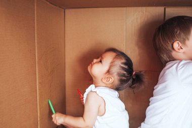 Güzel küçük çocuklar keçeli kalemlerle resim çizer ve kutularda oynarlar, evde çocuklar için etkinlik olur..