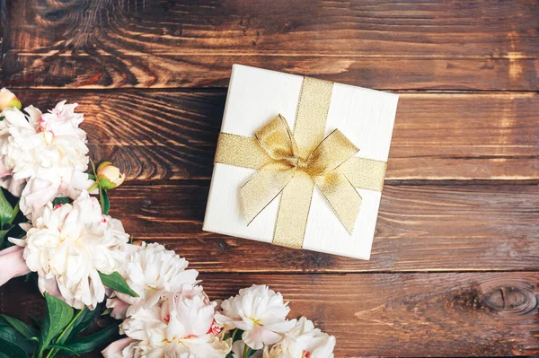 Belles pivoines délicates et une boîte cadeau blanche avec un arc sur un fond de bois, fleurs en fleurs, Mars 8, Fête des mères, cadeau d'anniversaire — Photo