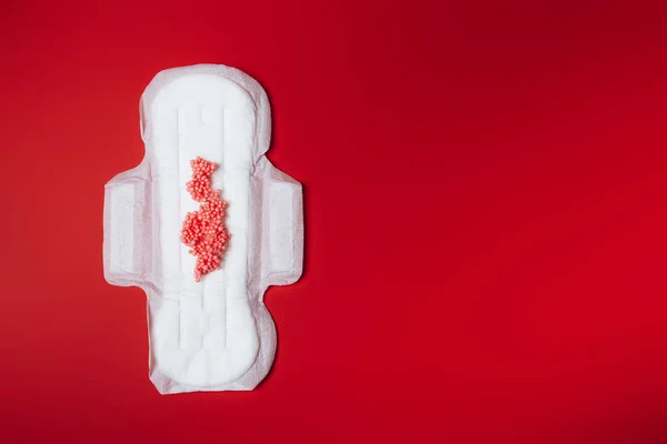 Serwetka sanitarna z czerwonymi kulkami imitującymi menstruację na czerwonym tle, opieka zdrowotna, ochrona miesięczna, niezawodny przyjaciel — Zdjęcie stockowe