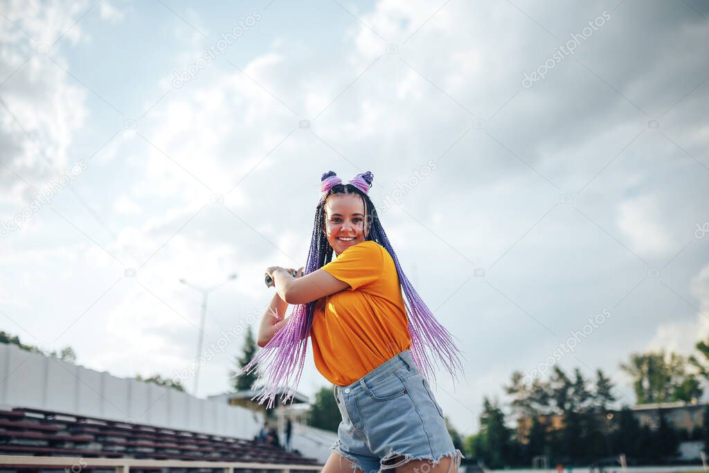 Young beautiful girl holding a baseball bat in a yellow open-air t-shirt in a sports stadium.