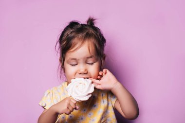 Güzel küçük kız pembe arka planda yumuşak bir krema yiyor, 8 Mart, anneler günü, doğum günü hediyesi, şekerler.