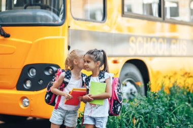 Sırt çantalı liseli kızlar okul otobüsünün arka planında kitap tutuyorlar, okula dönüyorlar.