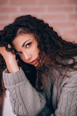 Kameraya poz veren kıvırcık saçlı ve kazaklı güzel bir kız.