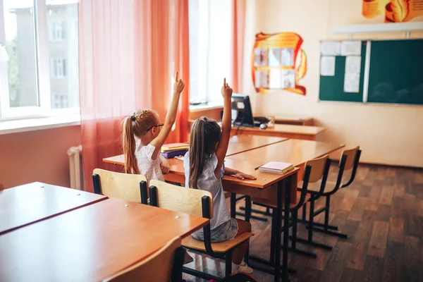 Дві Маленькі Школярки Сидять Столом Шкільному Класі Піднімають Руки — стокове фото