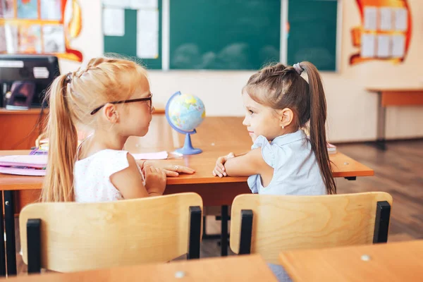 2人の女子学生が学校の机に座って授業の目的を話し合う — ストック写真