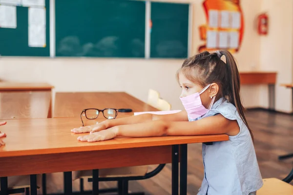 Two schoolgirls in medical masks are sitting at a school desk, opposite each other, group session, back to school, teaching children.