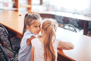 İki liseli kız bir okul masasında oturup dersin amacını tartışırlar..