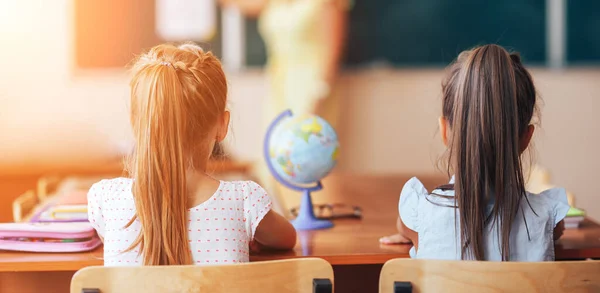 Дві Маленькі Школярки Сидять Столом Шкільному Класі Уважно Слухають Вчителя — стокове фото