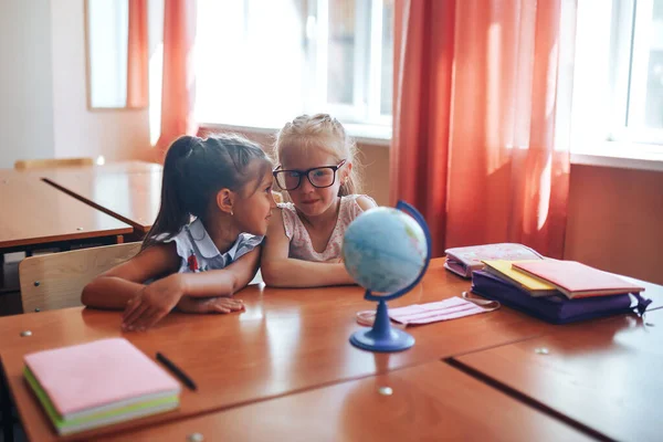 2人の女子学生が学校の机に座って授業の目的を話し合う — ストック写真