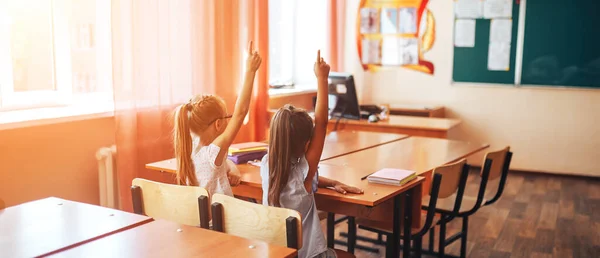 Дві Маленькі Школярки Сидять Столом Шкільному Класі Піднімають Руки — стокове фото