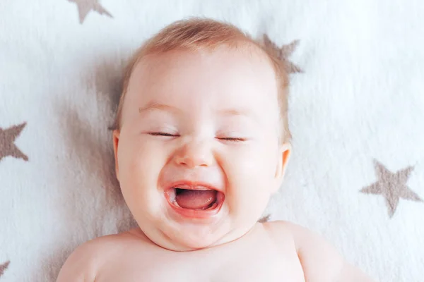 Фото емоційно веселого малюка, новонародженої дитини з блакитними очима і світлим волоссям, що лежить на світлій ковдрі з коричневими зірками — стокове фото
