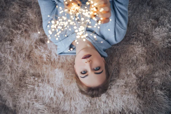 Молода блондинка в синьому светрі з садами в руках лежить на м'якому килимі "Веселого Різдва" і "Щасливого Нового Року". — стокове фото