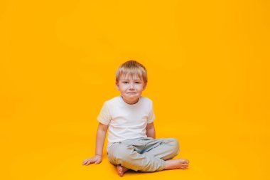 Ağlayan küçük çocuk elleriyle gözlerini ovuyor, sarı arka planda beyaz tişörtlü bir çocuk..