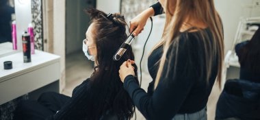 Sağlık maskeli kadın, salgın sırasında kuaförde saçını yaptırıyor..
