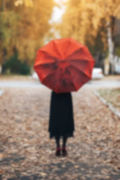 Femme marchant dans le parc par temps d'automne sous un parapluie rouge photo de fond floue est déconcentré — Photo