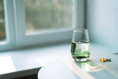 Glass of water with chlorophyll partially dissolved, soft green plumes. Capsules and softgels nearby. Horizontal wellness scene. High quality photo