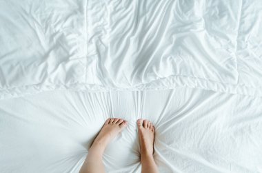 Ayak ve ayak parmakları şakayla yatağın beyaz kırışık çarşaflarına basıyor..