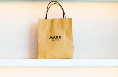 Maxx Coffee Shop 'tan beyaz desenli geri dönüşümlü kağıttan yapılmış kahverengi bir alışveriş çantasının önü..