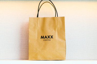 Maxx Coffee Shop 'tan beyaz desenli geri dönüşümlü kağıttan yapılmış kahverengi bir alışveriş çantasının önü..