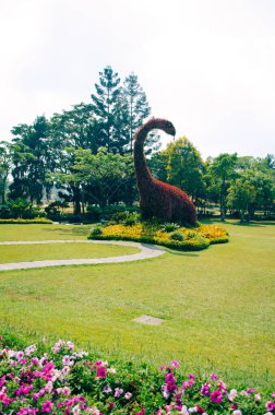 Bogor, Endonezya - Bulutlu bir öğleden sonra Taman Bunga Nusantara çiçek temalı parkın manzarası otçul bir dinozor şeklindeki bir çalılığa bakıyor.