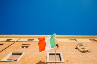 Roma, İtalya - Solda hareket eden ve arka planda açık gökyüzü olan bir apartman dairesinde direğe bağlı bir İtalyan bayrağının minimalist üst görüntüsü.