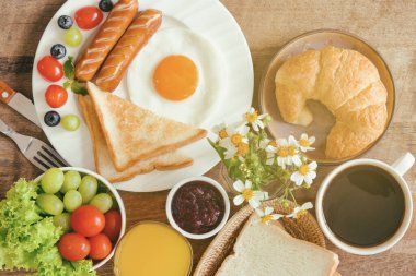 Sunny Side ile ev yapımı kahvaltı kızarmış yumurtalı tost sosis sebzeli kruvasan çilekli reçelli kahve ve portakal suyu düz konsepsiyonda. Aile için nefis Amerikan kahvaltısı..