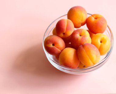 Pembe arka planda cam bir kasede olgun kayısılar. Yakın plan.