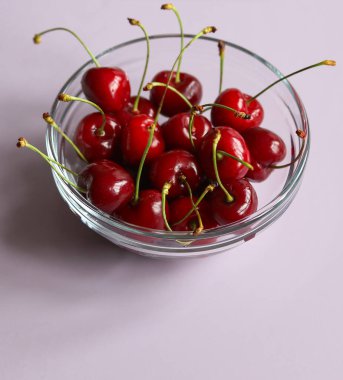 Olgun, sulu kirazlar cam kasede, eflatun arka planda bir makro fotoğrafta.