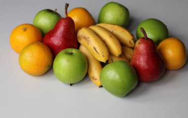 Kırmızı armutlar, sulu yeşil elmalar, taze mandalinalar ve beyaz arka planda olgun muzlar.