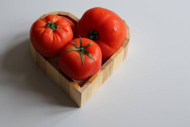 Kalp şeklinde ahşap bir kasede büyük kırmızı domatesler. Yaklaş.