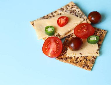 Kuru kurabiye ve peynirli dilimlenmiş domates ve mavi arka planda kırmızı biber.